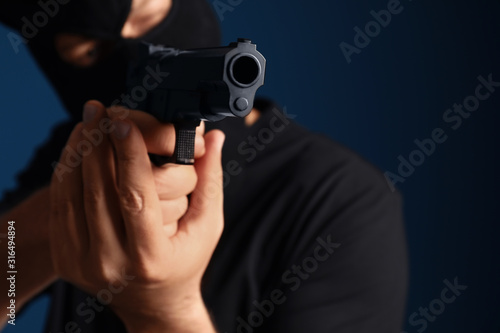 Man in mask holding gun against dark blue background, focus on hands © New Africa