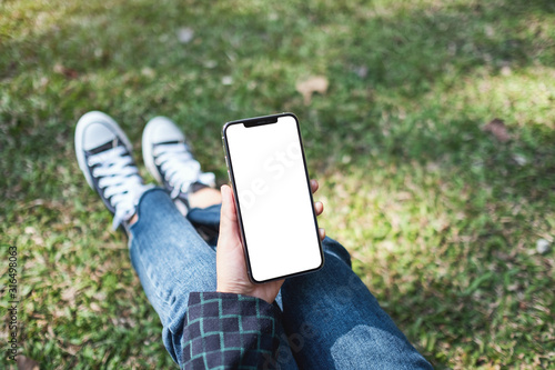 Mockup image of a woman holding black mobile phone with blank white screen while sitting in the outdoors photo