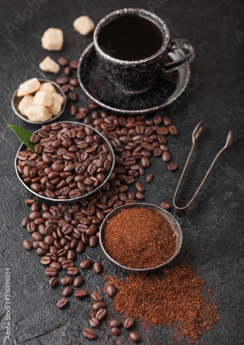 Cup of fresh raw organic coffee with beans and ground powder with cane sugar cubes with coffee tree leaf on black background. Top view