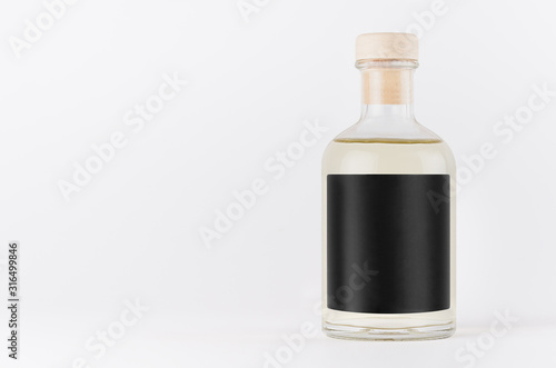 Transparent glass bottle for cosmetic, perfume, alcohol drink with black label, cork, yellow liquid on white background, mock up for design.