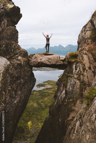 Brave woman traveler standing on hanging stone between rocks adventure vacation travel healthy lifestyle hiking outdoor success balance concept Djevelporten in Norway Lofoten islands