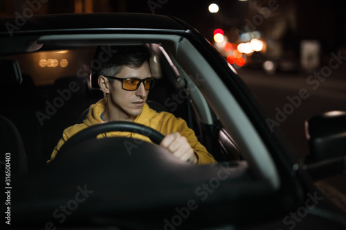 Obraz na plátně Man driving car in special yellow eyeglasses at night for good night vision