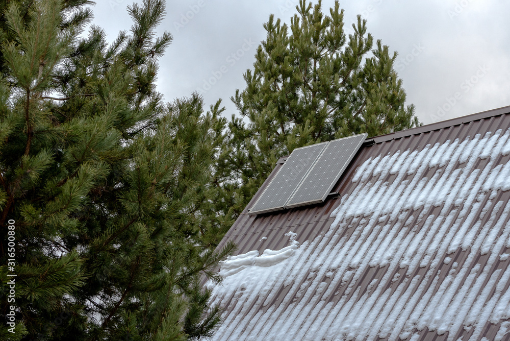 Two solar panels on the snow-covered roof of the house. Two solar panels on the snow-covered roof of the house.