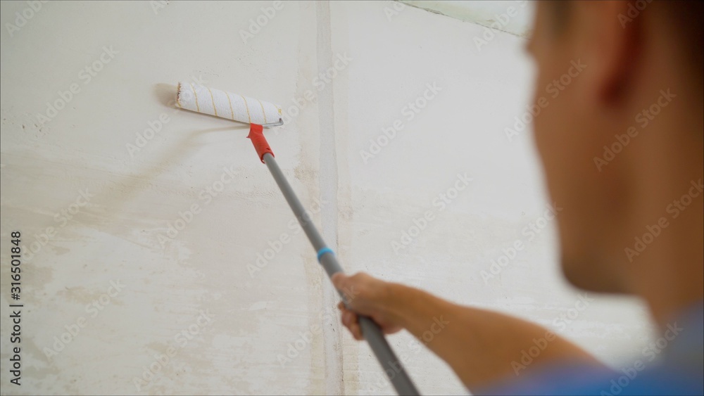 Worker in a blue suit is processing the wall. Worker plastering a wall. Worker with a roller Worker in a blue suit is processing the wall. Worker plastering a wall. Worker with a roller