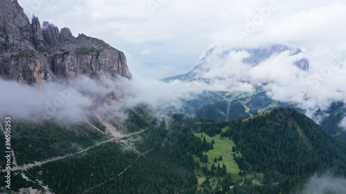 Aerial view of Dolomites in fog  low clouds. Road goes along dolomite cliffs and fir tree forest. South Tyrol  Italy. Beautiful landscape.