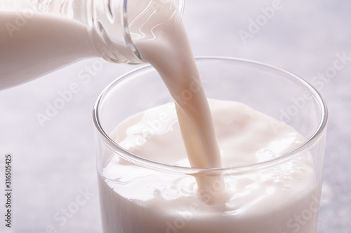 Fotografie, Obraz Pouring milk from bottle into a glass on light blue background, high key shot