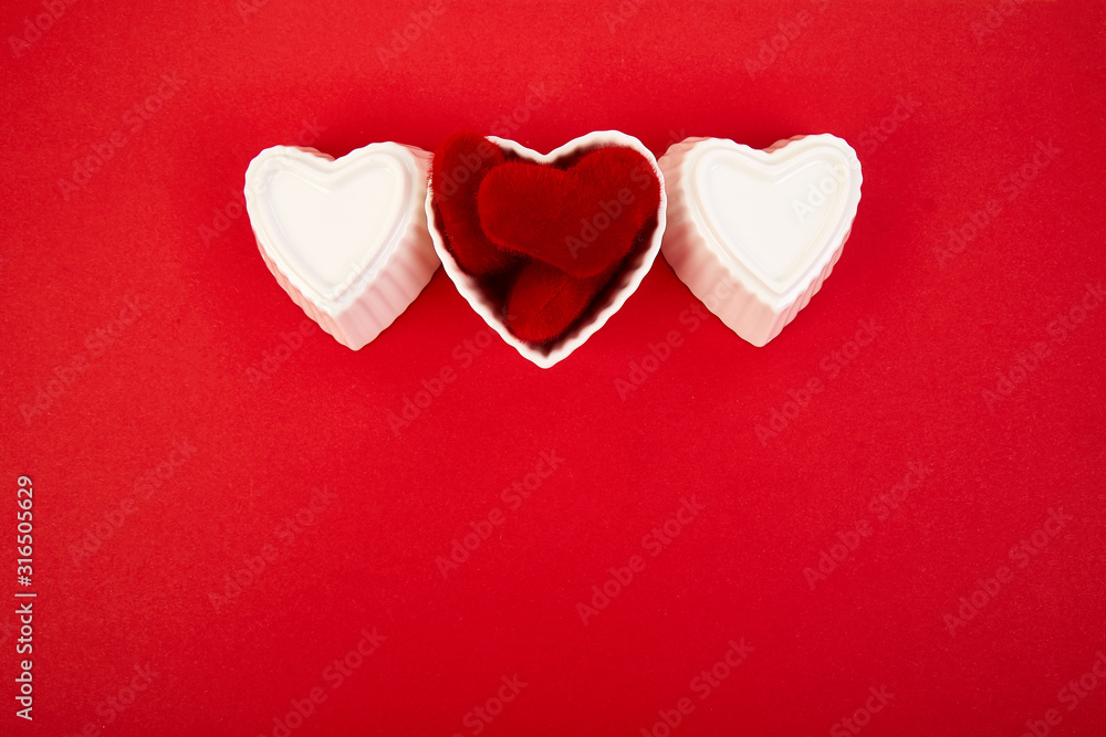 White ceramic hearts with red plush  hearts on red background. Flat lay composition. Romantic, St Valentines Day concept. Love. Copy space.