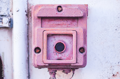 Black button in a large red case with faded pink paint on an old wall.