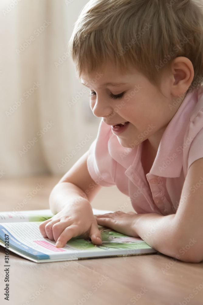 A cute little child, lying on the warm home floor, reading an interesting story in a huge book. A cute little child, lying on the warm home floor, reading an interesting story in a huge book.
