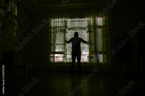 Silhouette of a man standing at a window inside the room. Fantasy picture with old vintage lantern at the window inside dark room.