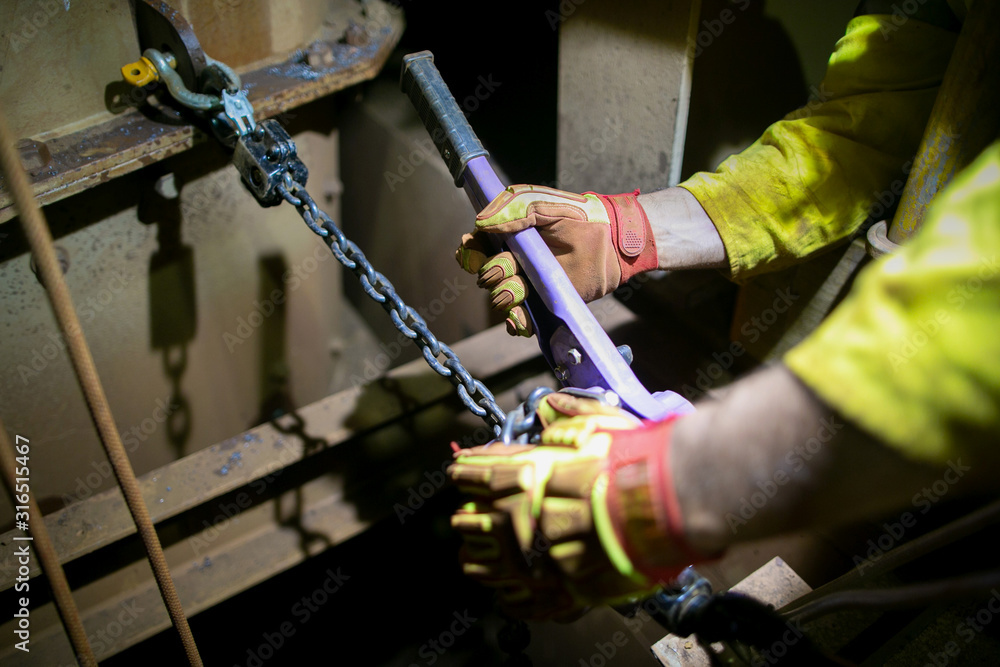 Industrial rigger wearing safety glove inspecting pulleys equipment 1 Tone purple come along hooking on 2 tones shackle prior used Industrial rigger wearing safety glove inspecting pulleys equipment 1 Tone purple come along hooking on 2 tones shackle prior used
