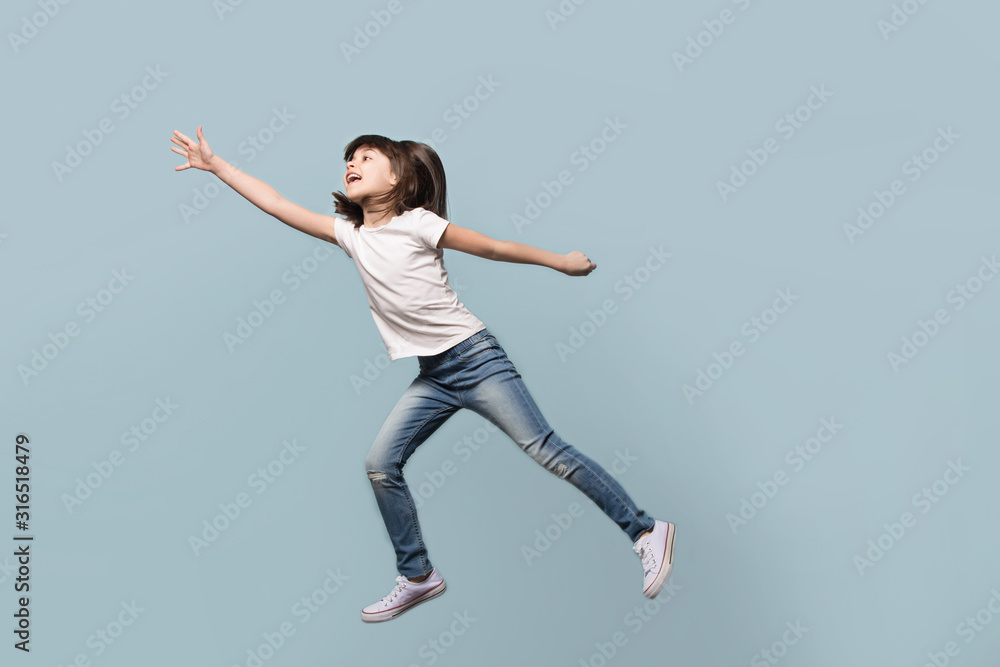Happy little preschool girl jumping on blue background.