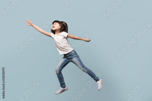 Happy little preschool girl jumping on blue background. © fizkes