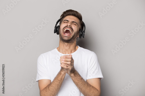 Overjoyed young guy imitating singing in microphone, wearing headset.