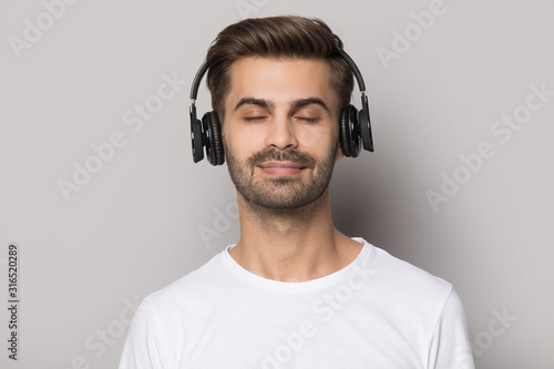Handsome guy wearing modern wireless headphones, enjoying favorite slow music.
