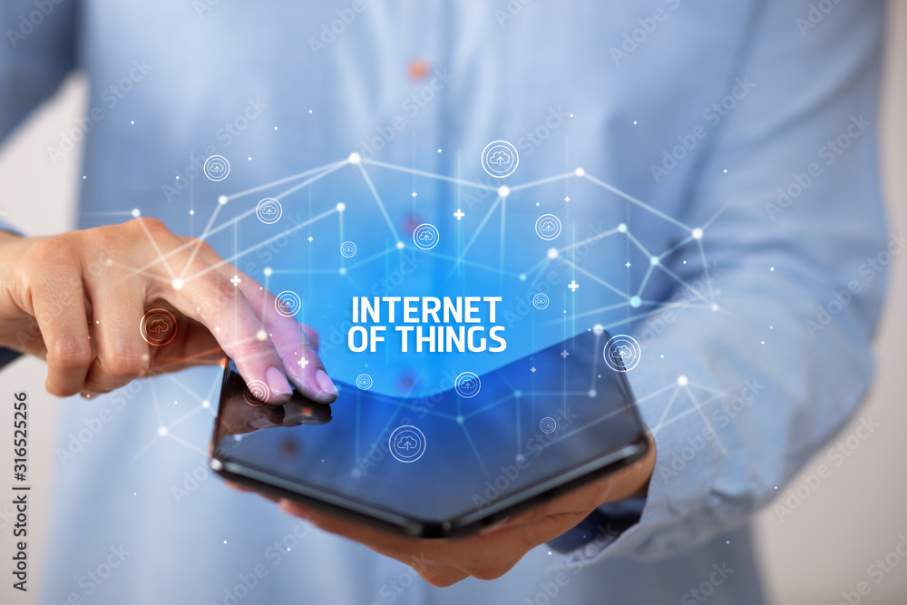 Businessman holding a foldable smartphone with INTERNET OF THINGS inscription, new technology concept Businessman holding a foldable smartphone with INTERNET OF THINGS inscription, new technology concept