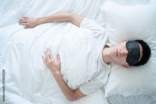 asian young man sleeping in bed with an eye mask in bedroom