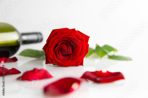 Leżąca czerwona róża na białym tle, płatki i butelka wina