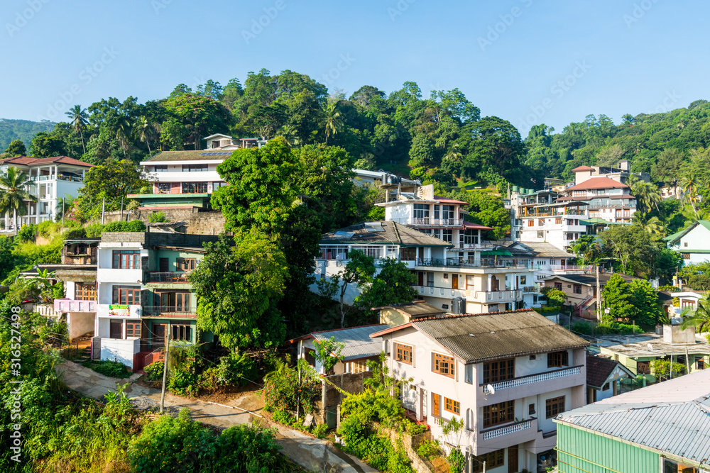 Fototapeta premium Beautiful builings on the green hills in the downtown, nex to the Kandy Lake or Kiri Muhuda or the Sea of Milk, an artificial lake in the heart of the hill city of Kandy, Sri Lanka