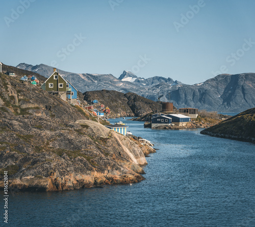 Colorful houses dot the hillsides of the fishing town of Kangaamiut, West Greenland. Icebergs from Kangia glacier in Greenland swimming with blue sky and clouds. Symbol of global warming. © Mathias