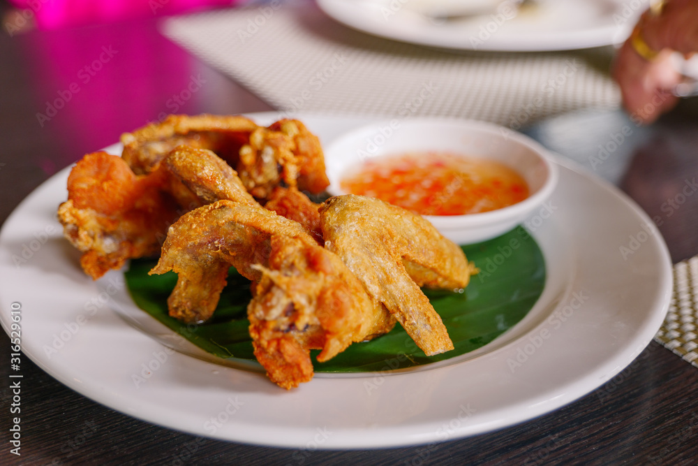Thai style deep fried crispy chicken wing, serve on white dish with spicy sweet sauce on side. Thai famous appetizer dish. Thai style deep fried crispy chicken wing, serve on white dish with spicy sweet sauce on side. Thai famous appetizer dish.