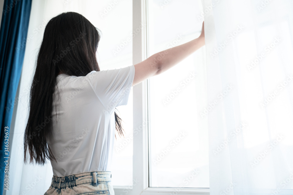 asian young woman open curtains in bedroom in the morning asian young woman open curtains in bedroom in the morning