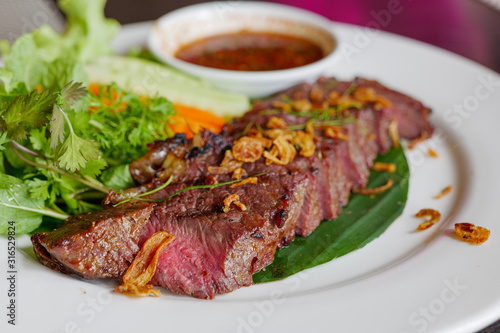 Slice medium rare grilled beef steak on top with fried garlic with Thai spicy sauce and vegetable on side.