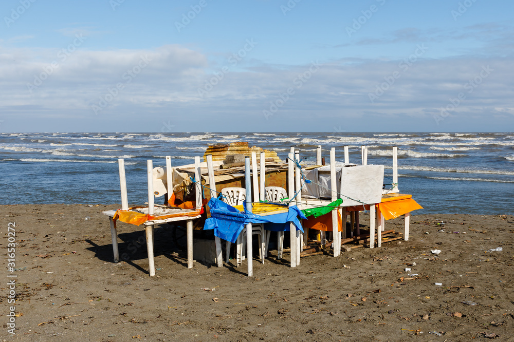 plastic tables and chairs stacked on the sandy seashore before the storm, Caspian Sea, Iran