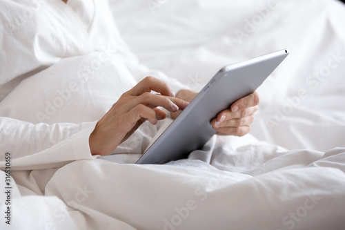 Close up woman holding tablet pc, sitting in bed