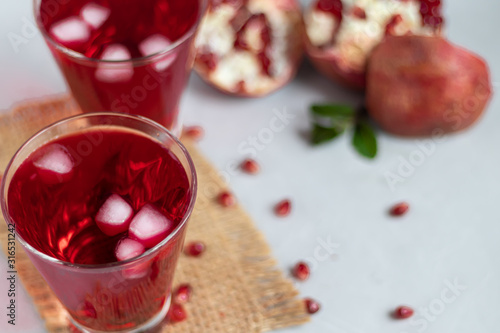 Pomegranate juice in transparent glasses. On a light background under a stone. Trend 2020. Grains are scattered nearby.