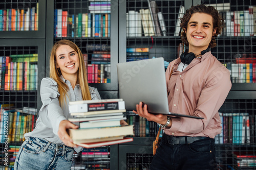 Young​ stidents standing​ outside​ library and holding the​ laptop​ and books. photo