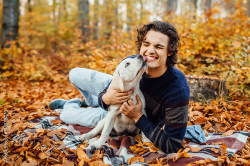 Photo of handsome man and his  labrador playing together in the autumn forest.