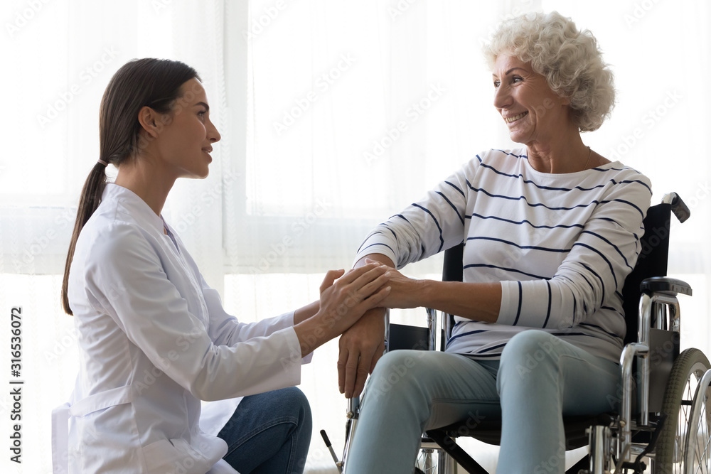 Caring nurse comforting disabled older woman sitting in wheelchair Caring nurse comforting disabled older woman sitting in wheelchair