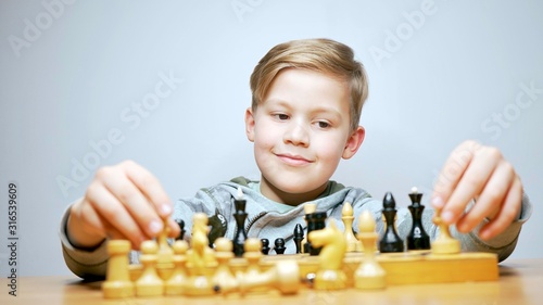 Happy beautiful boy playing chess. Caucasian child thinks while playing chess boardgame. White background                             