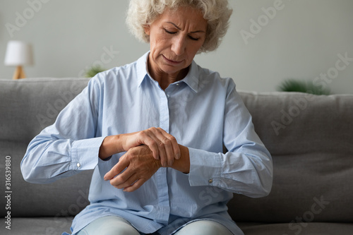 Unhappy older woman massaging wrist, feeling pain in joint