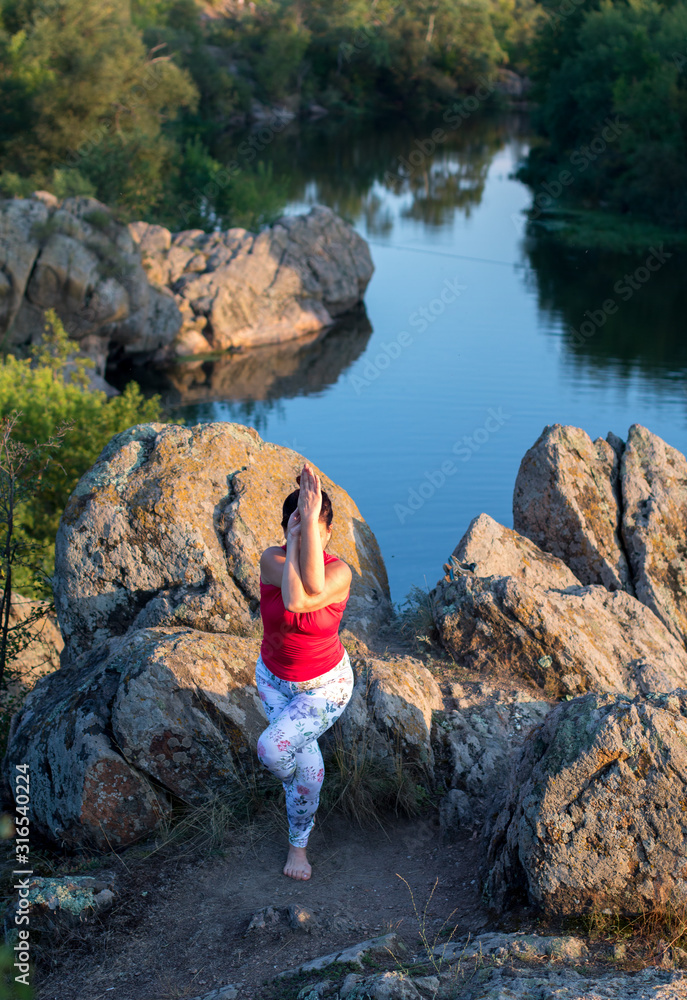 adult woman doing yoga asanas on the rocks above the river