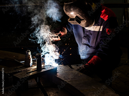 worker welds metal structures by electric arc welding