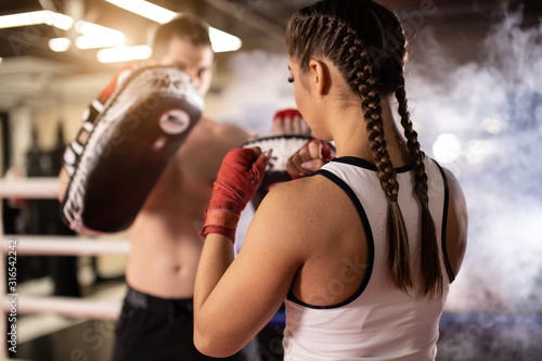 young sportive fit couple training together in ring, man with naked torso and woman in sportive wear, wearing red protective bandages on hands. Boxing, sport concept. Smoky space