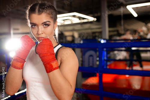Professional caucasian female fighter in ring. Young beautiful fit woman in red boxing bandages ready to fight opponent in boxing ring, wearing sportive clothes © alfa27