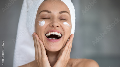 Close up excited beautiful woman laughing, applying moisturizing cream