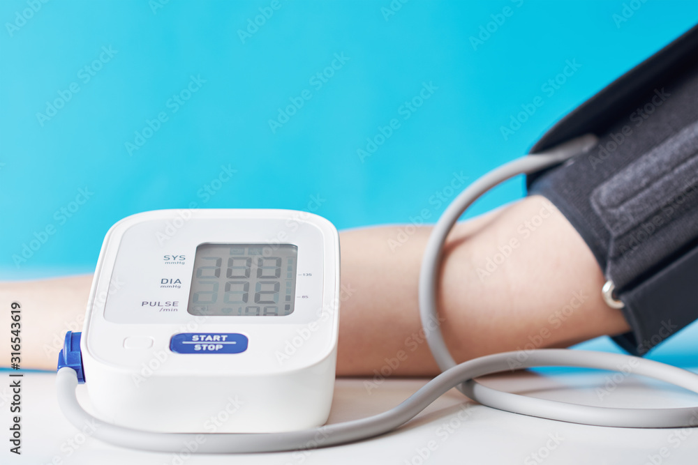 Woman measuring blood pressure with a digital pressure monitor against blue background. Health care and medical concept Woman measuring blood pressure with a digital pressure monitor against blue background. Health care and medical concept