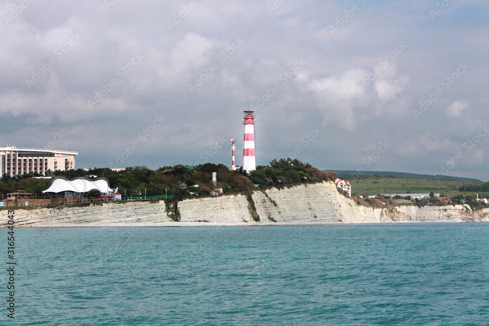 Coastal lighthouse on the edge of a rocky promontory in the black sea, the city of Gelendzhik. Located to the left of the frame. Landscape. Horizontal photo. Blurred background. Summer. opy space
