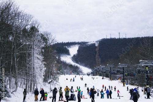 Looking at crowd at bottom of ski slope getting in line for ski lift.  With people skiing in distance. 