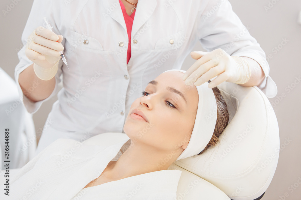 Unidentified master cosmetologist makes botox injections into the eyebrow of a beautiful young woman client. The concept of rejuvenating aesthetic procedures Unidentified master cosmetologist makes botox injections into the eyebrow of a beautiful young woman client. The concept of rejuvenating aesthetic procedures