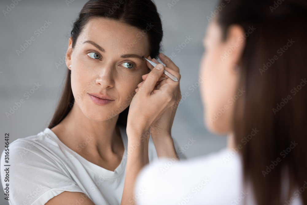 Beautiful woman tweezing eyebrows close up, looking in mirror Beautiful woman tweezing eyebrows close up, looking in mirror