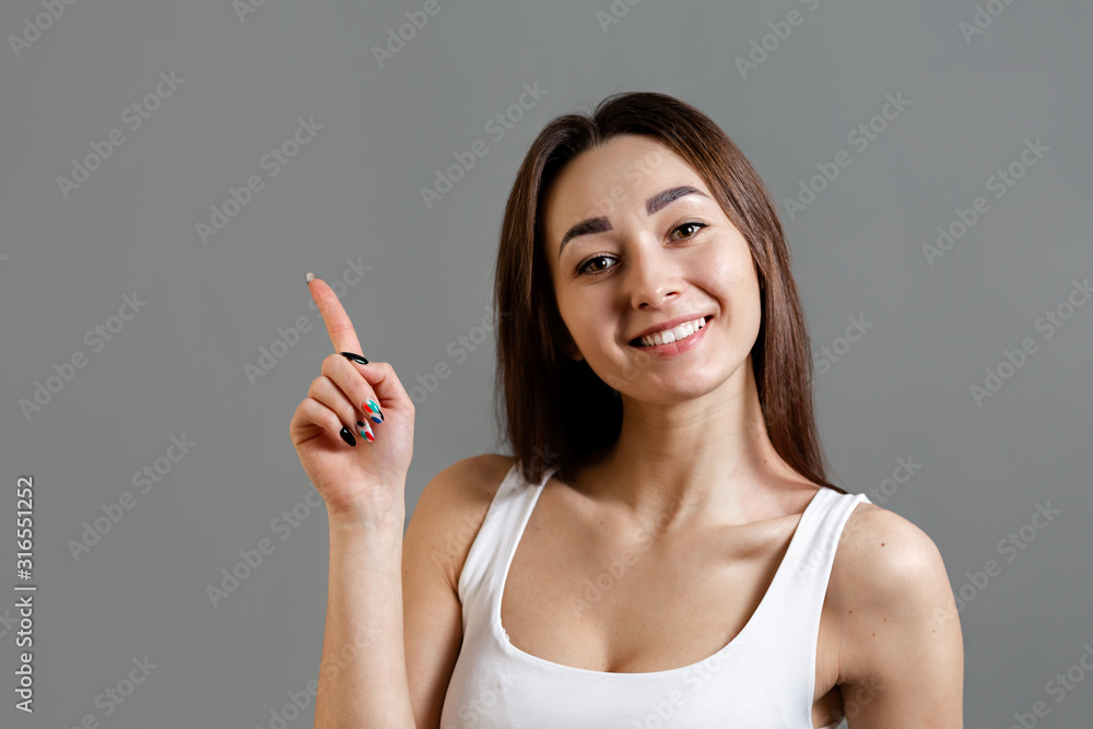 Concept of idea and information search. Portrait of a happy young Caucasian woman with a smile pointing her finger up. Gray background. Copy space Concept of idea and information search. Portrait of a happy young Caucasian woman with a smile pointing her finger up. Gray background. Copy space