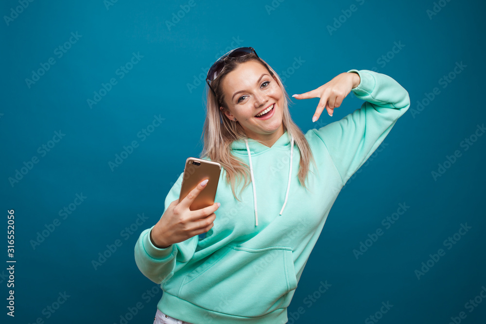 Fototapeta premium Stylish trendy hipster girl in the blue hoodie with the hood uses a smartphone.