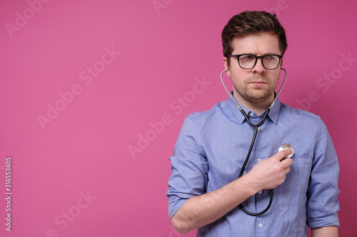 Serious caucasian worried man listening to his heart with stethoscope photo