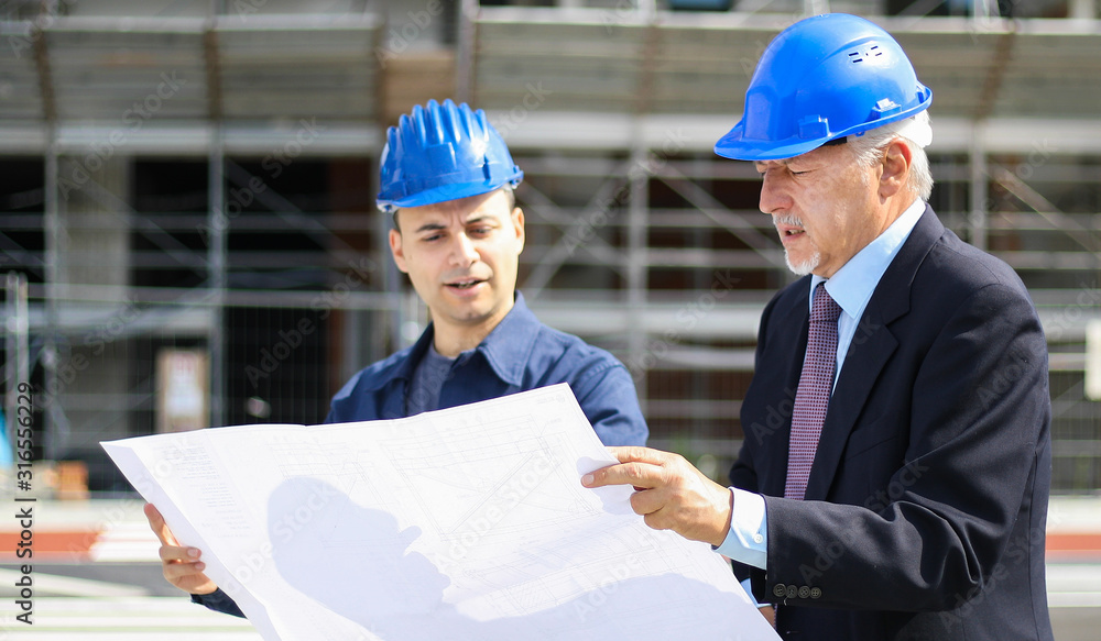 Two architect developers reviewing building plans at construction site Two architect developers reviewing building plans at construction site