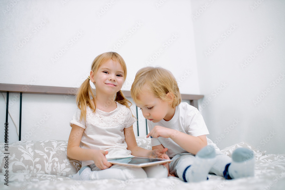attractive caucasian children using modern gadget, playing and looking on tablet, interested in modern technologies and gadgets, wearing white casual domestic clothes attractive caucasian children using modern gadget, playing and looking on tablet, interested in modern technologies and gadgets, wearing white casual domestic clothes